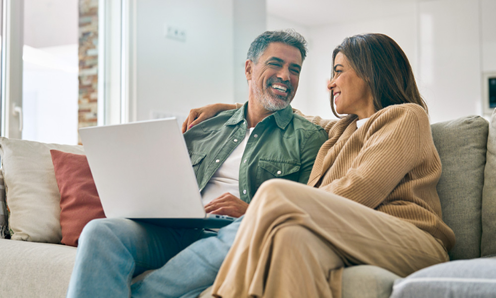 Image_Happy-Couple-Couch-Computer_1000x600px Happy couple sitting on couch looking at a laptop.