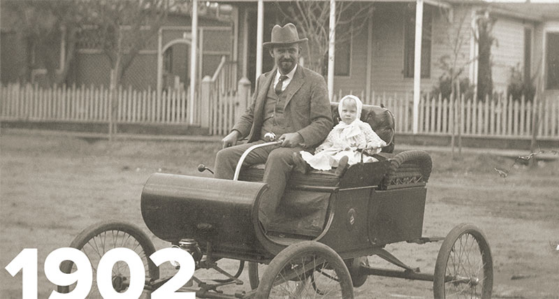 Old image of man in old car with child next to them